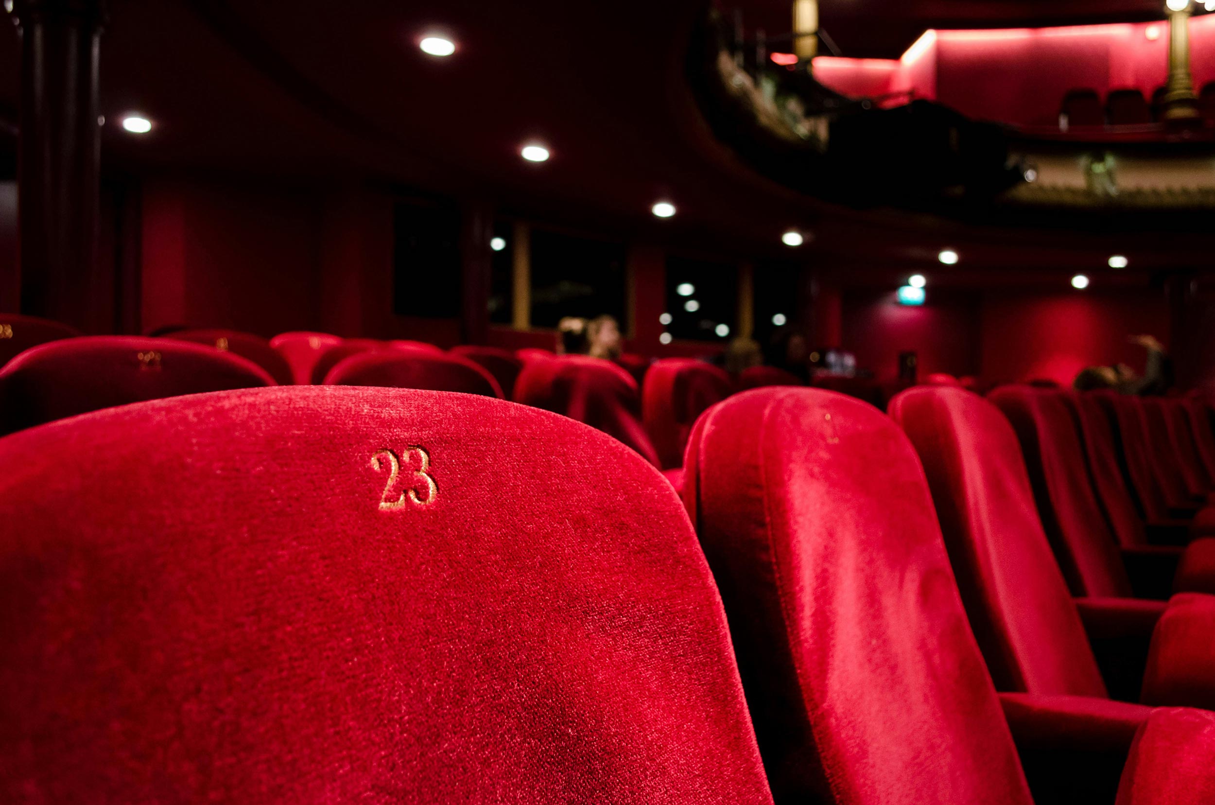 A close-up of red velvet theater seats in a dimly lit cinema.