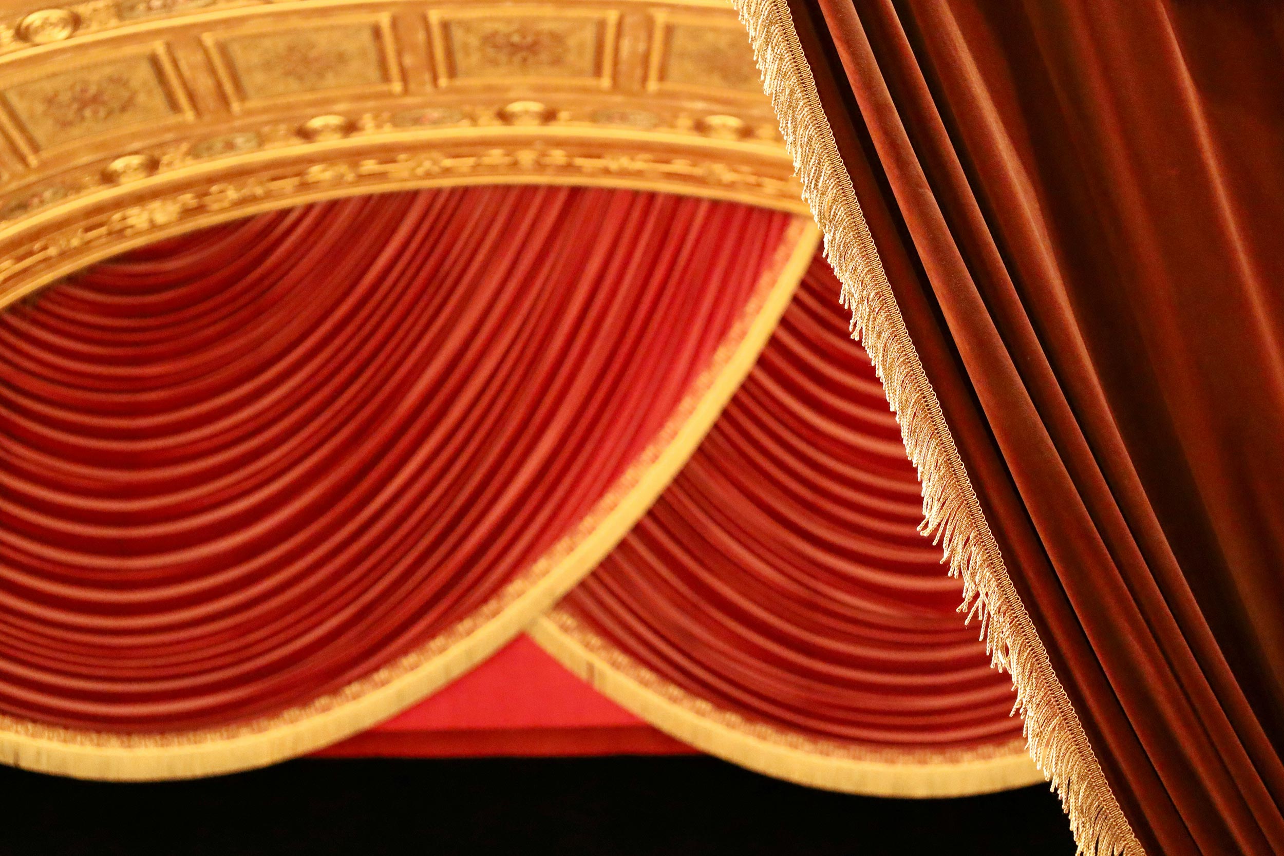 Elegant red velvet theater curtains with gold trim and ornate ceiling detail