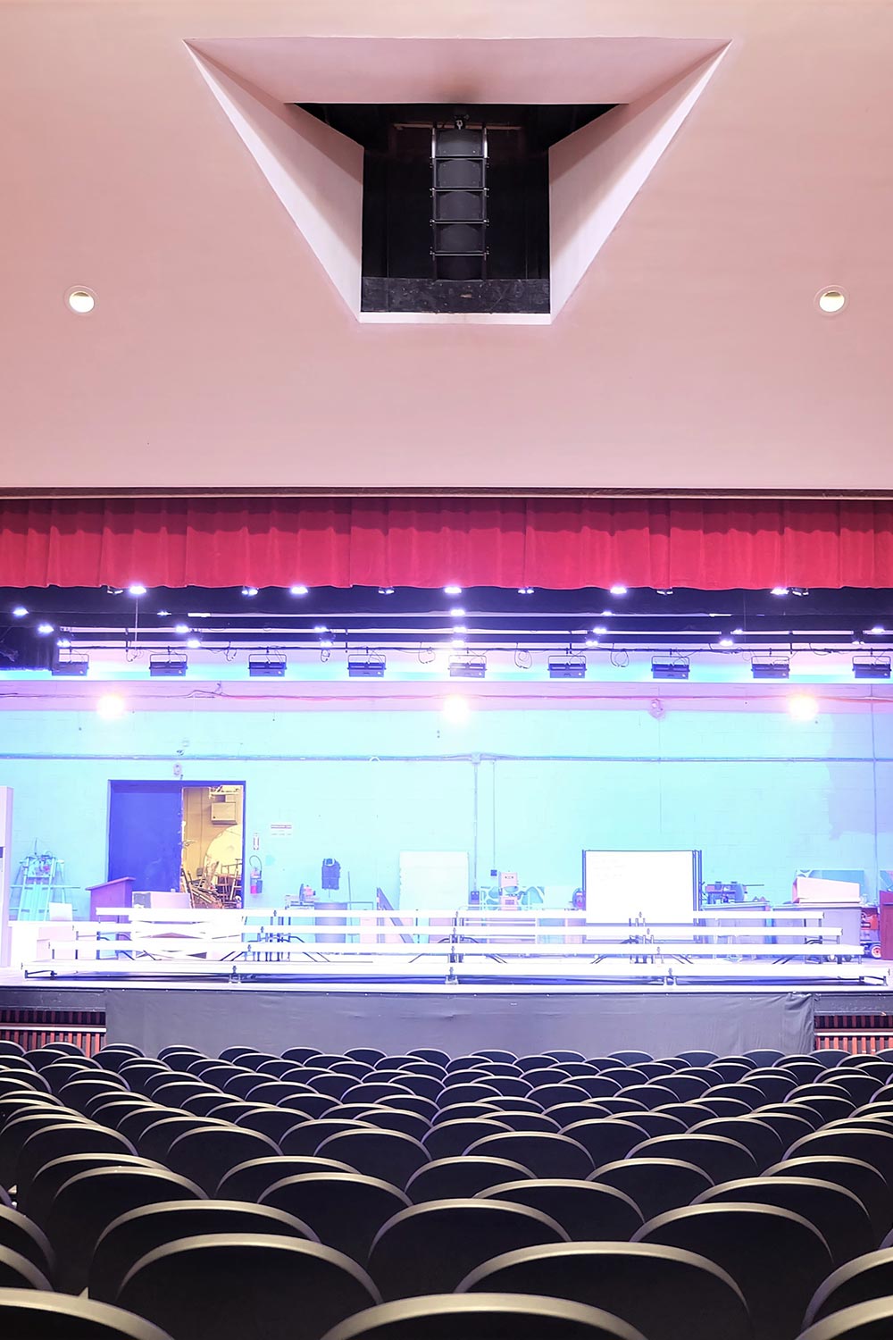 Auditorium view of stage with red curtain, overhead lights, and rows of empty seats
