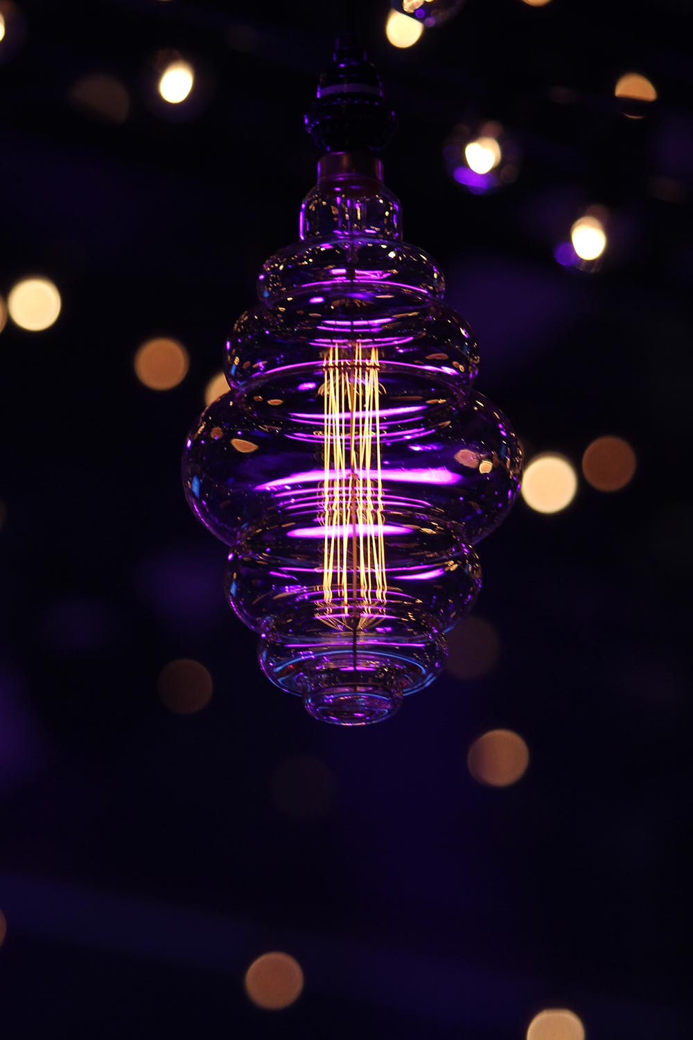 Close-up of a decorative glass light bulb glowing purple with string lights in background
