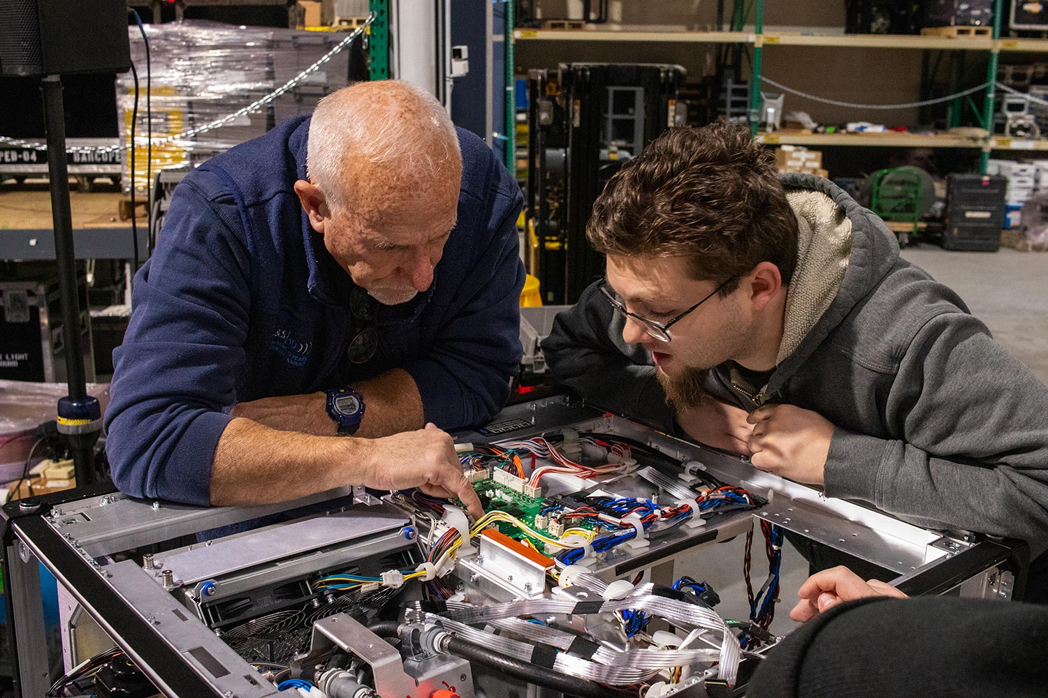 Two technicians examining and troubleshooting the wiring of a complex machine