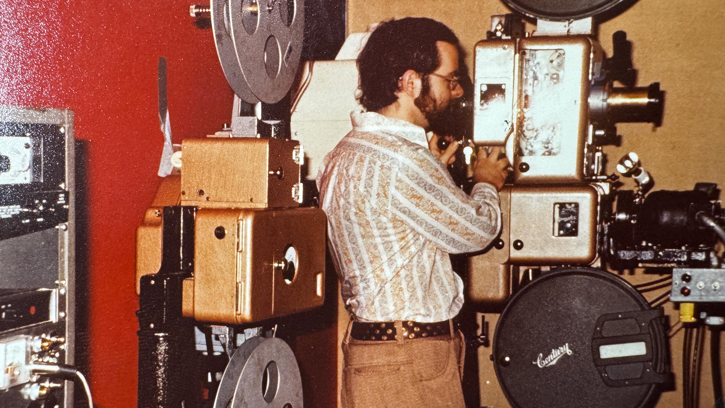 Man operating a film projector with large reels in a retro control room