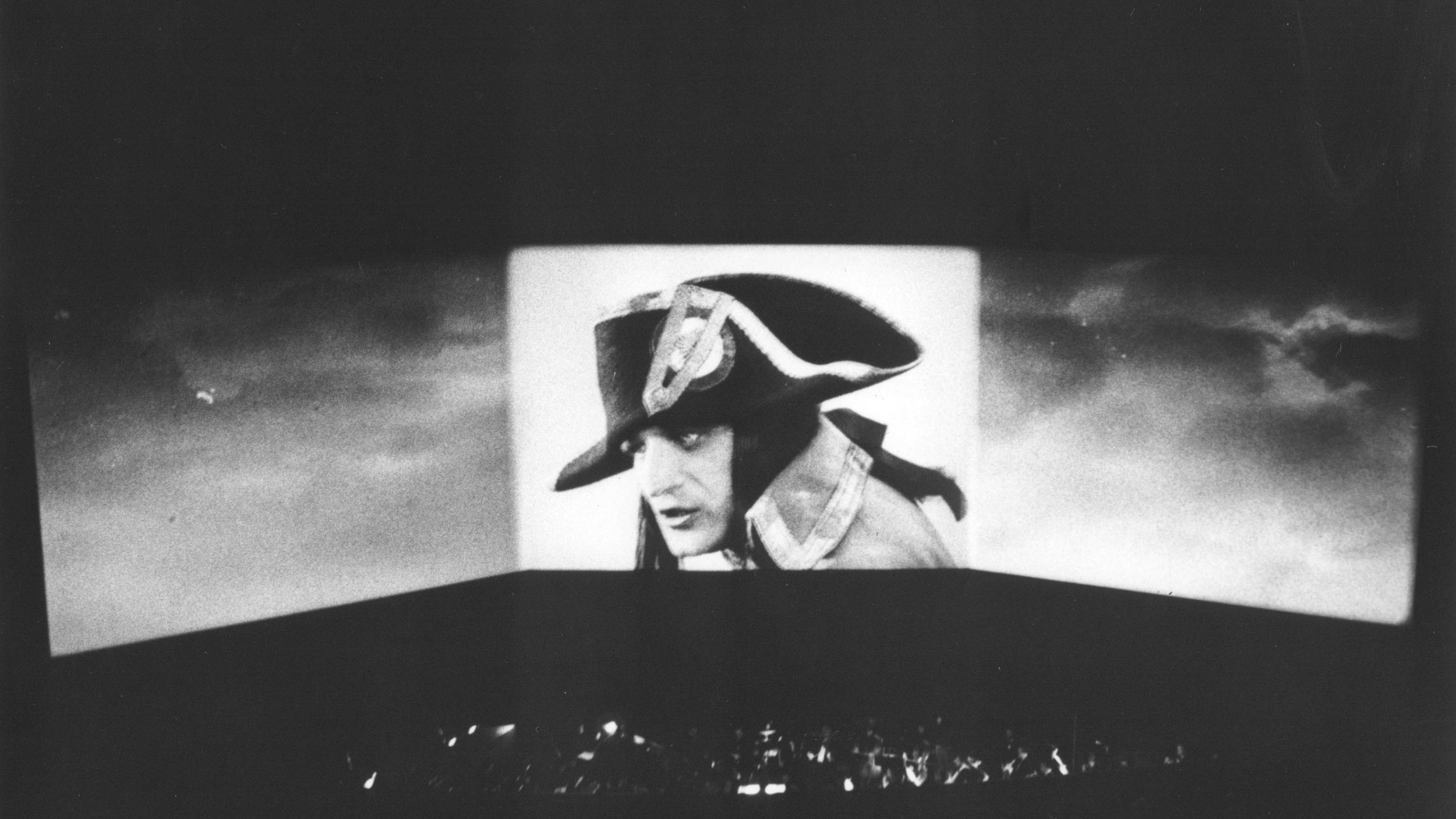 Scene from a film featuring a man in a Napoleon hat projected across a wide screen