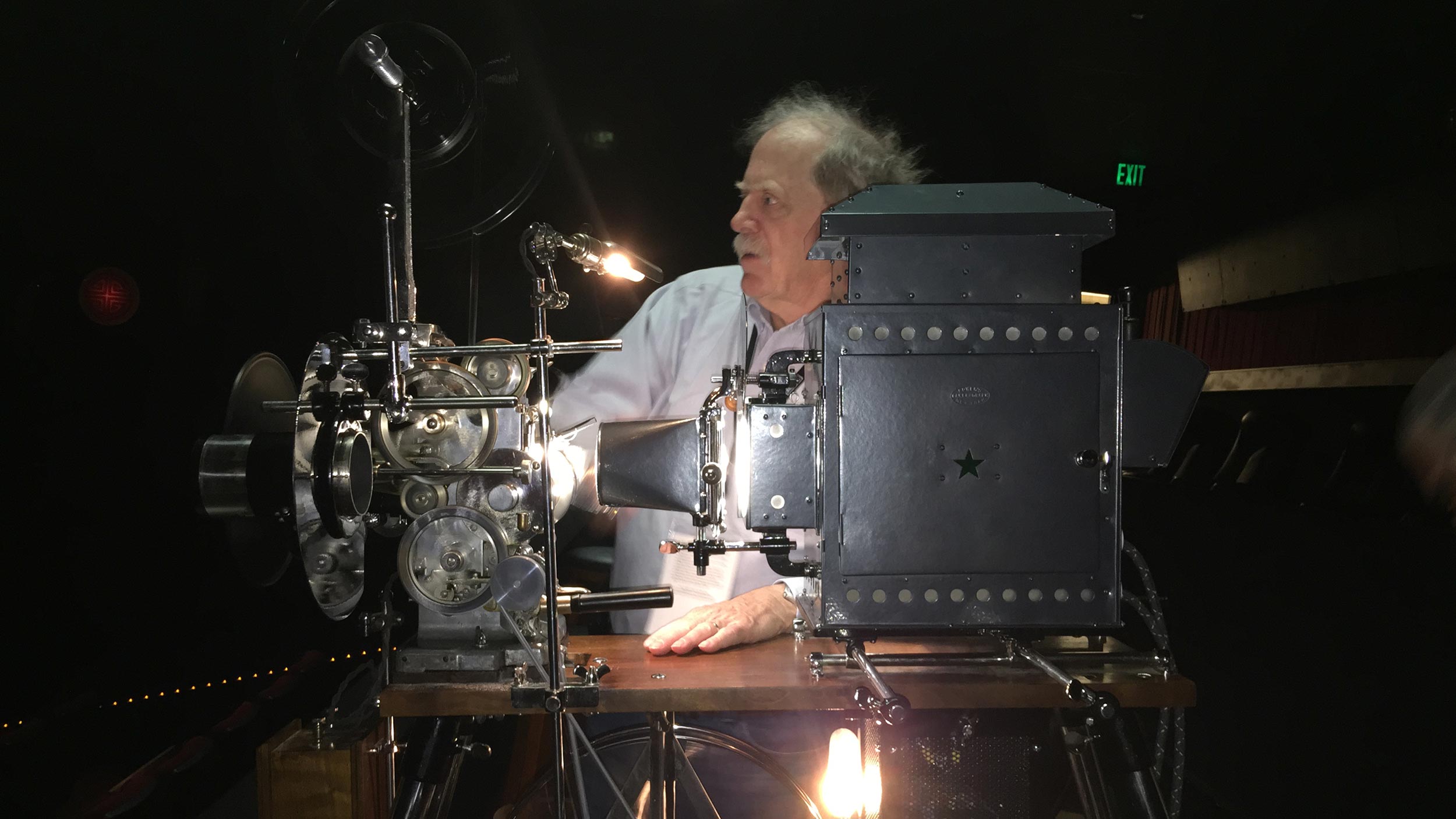 Man operating a vintage film projector in a dark theater