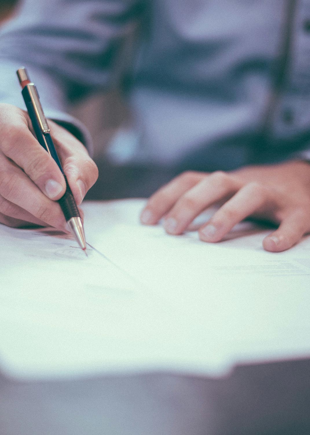 A close-up of a person signing a document with a pen.