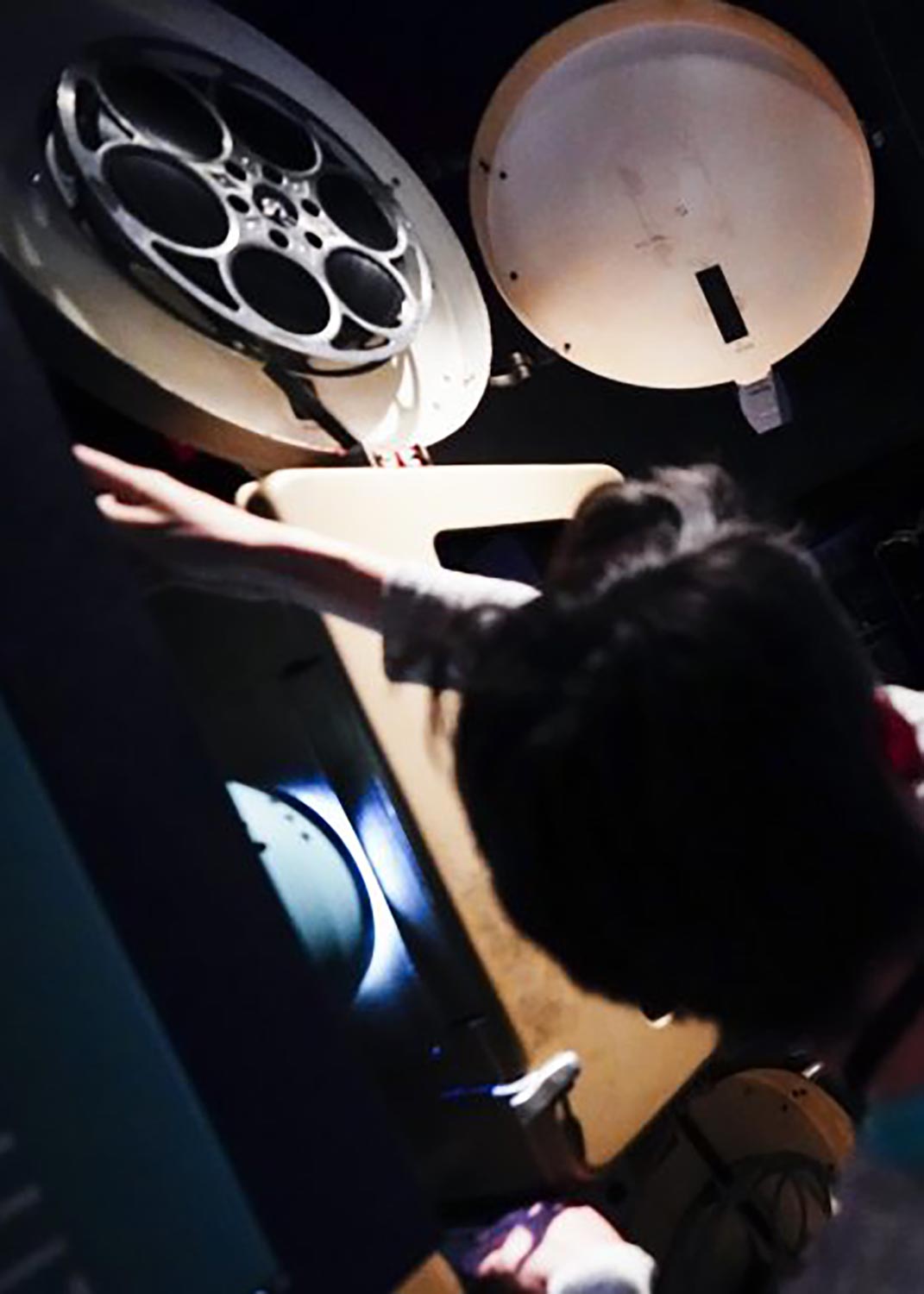 A person working on a film projector with a large film reel.