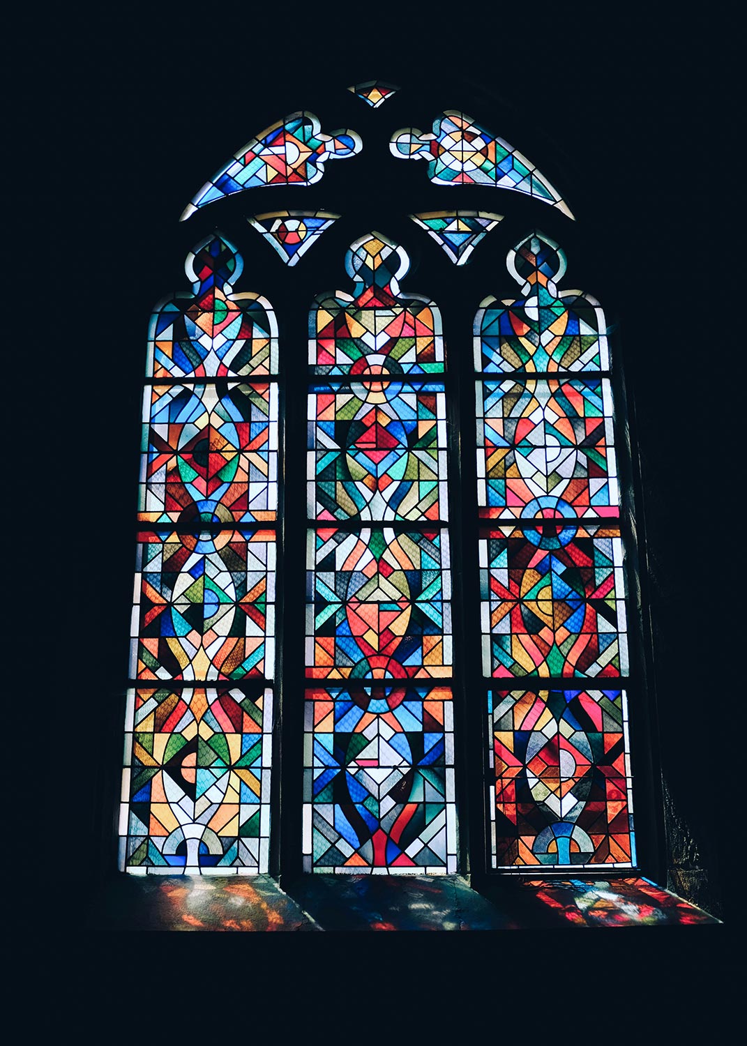 A stained glass church window with intricate patterns and vibrant colors letting in sunlight.