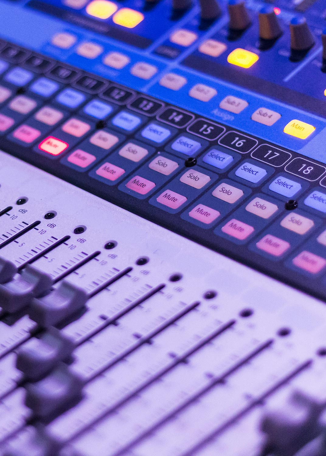 A close-up of an audio mixing console with multiple sliders and colorful buttons.