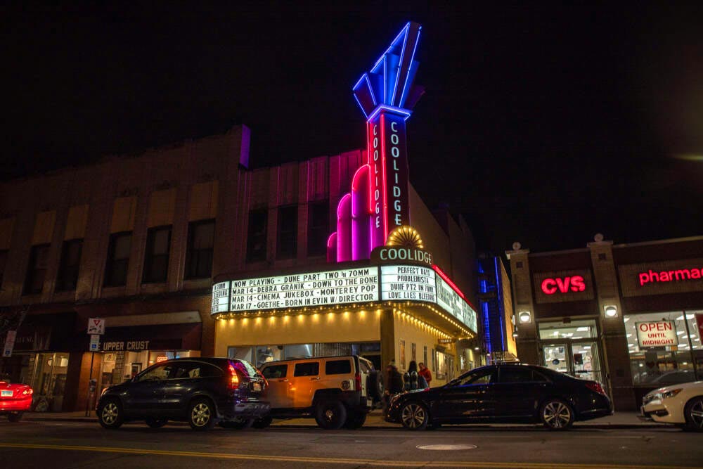 Night view of Coolidge Corner Theatre with neon lights and marquee listing film showtimes