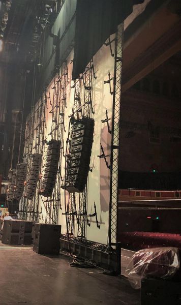 Backstage view of audio equipment behind a giant screen