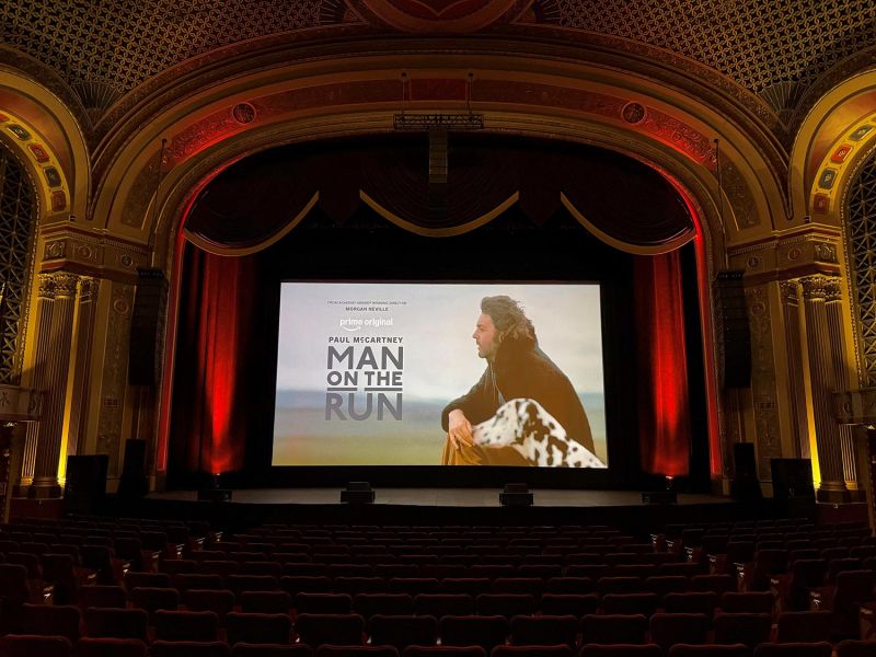 Movie poster displayed on a screen inside a large, ornate theater with red velvet seats