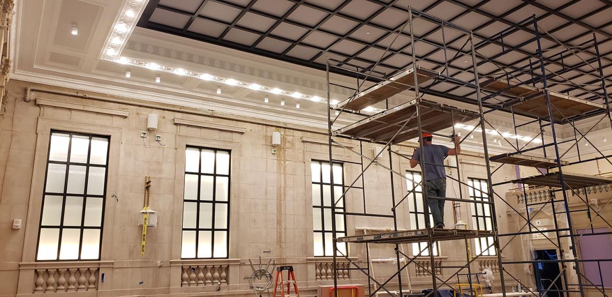 Technician on scaffold working on ornate ceiling in a large ballroom