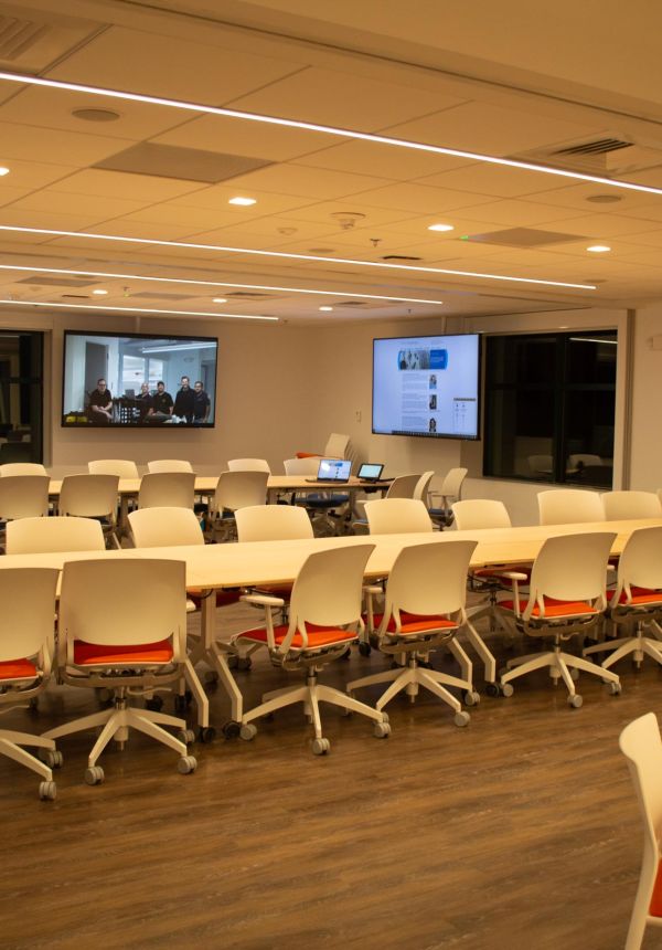 Modern classroom with white chairs, wood floors, and large screens on walls