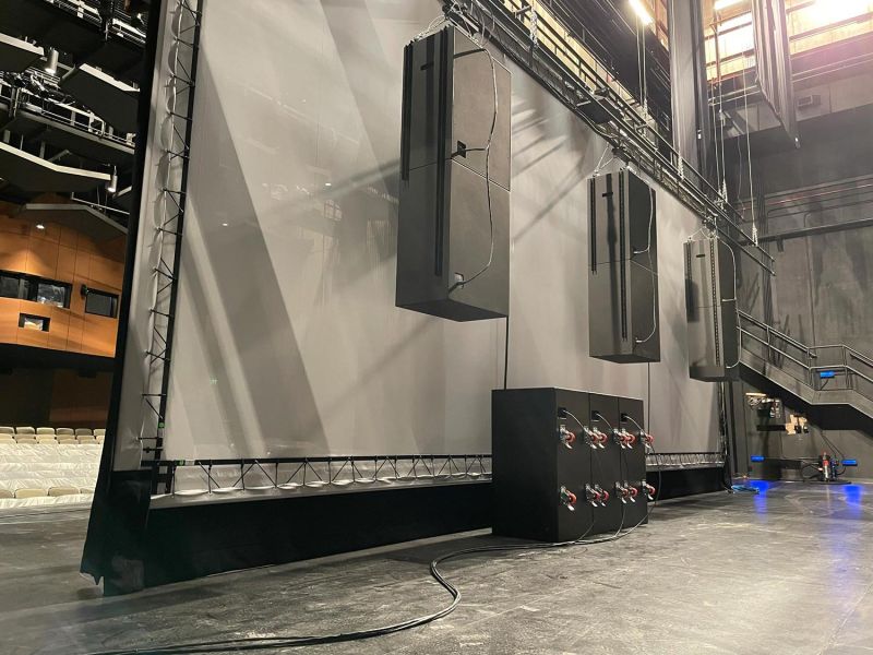 Backstage view of a theater with large speakers suspended beside the screen