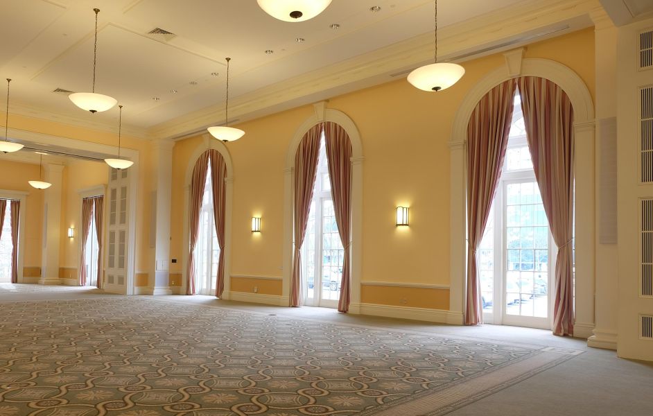 Spacious event hall with arched windows, soft yellow walls, and hidden audio panels