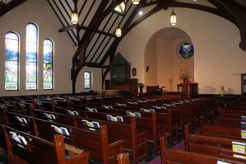 Interior of church with wooden pews, stained glass windows, and organ pipes