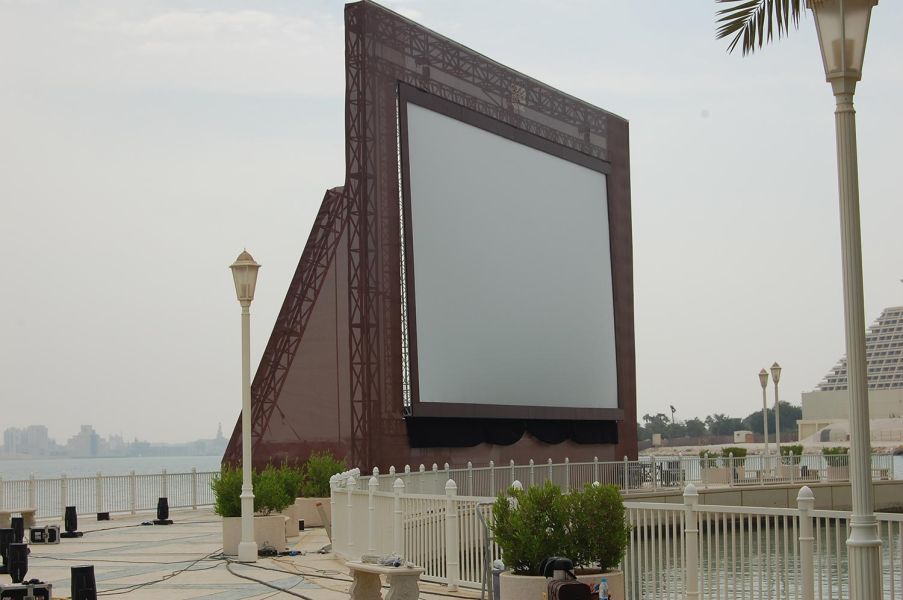 Large outdoor movie screen beside waterfront with lamp posts