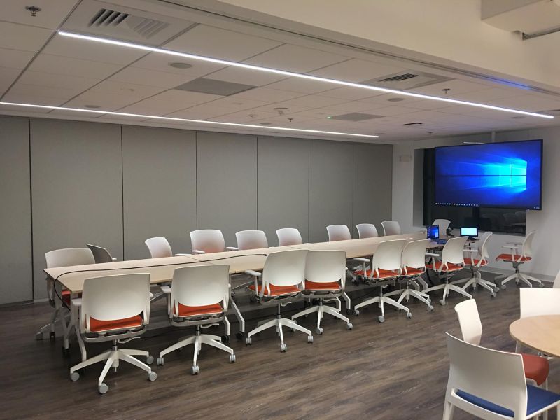 Conference room setup with long tables, rolling chairs, and large display