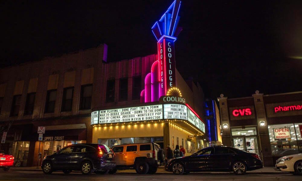 Night view of Coolidge Corner Theatre with neon lights and marquee listing film showtimes