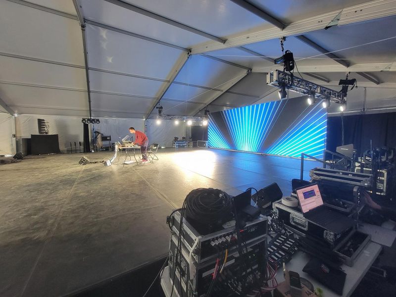 Person preparing sound system under a large tent with LED screen