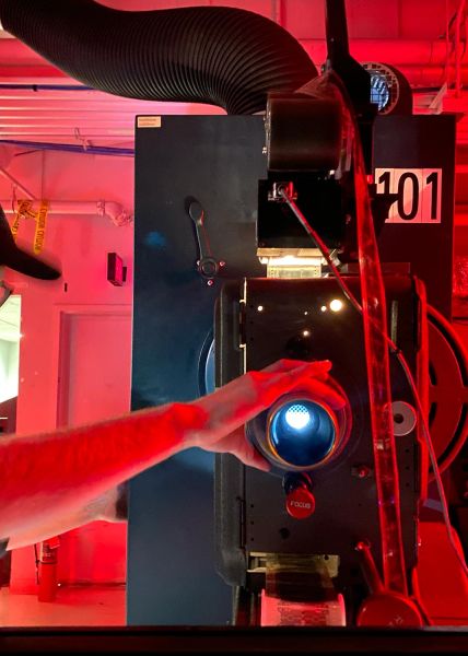 Technician adjusting a film projector in a room lit with red lighting